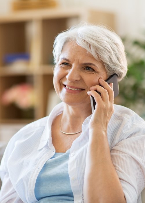 Smiling senior woman using her cell phone to contact dental office in Cumming