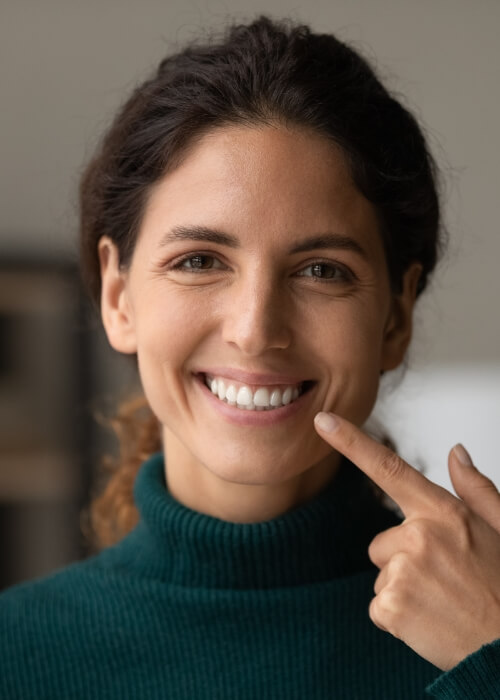 Brunette woman pointing to her smile after cosmetic dentistry in Cumming