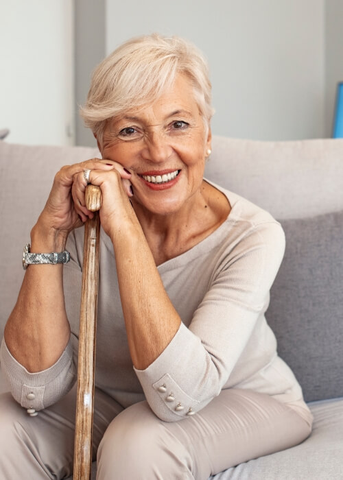 Senior woman on couch leaning on her cane and smiling after denture reline and repair in Cumming