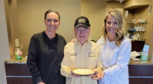 Two dental team members smiling with a senior man holding a pie