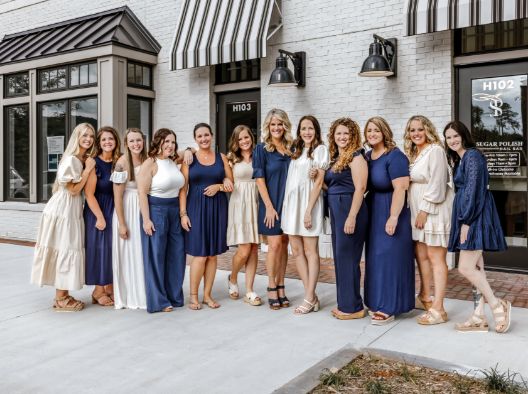 Bragg Dental team members in dresses standing outside of restaurant with white brick wall