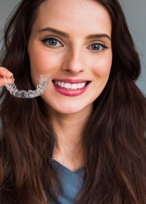 Smiling woman holding a Clear Correct clear aligner in Cumming