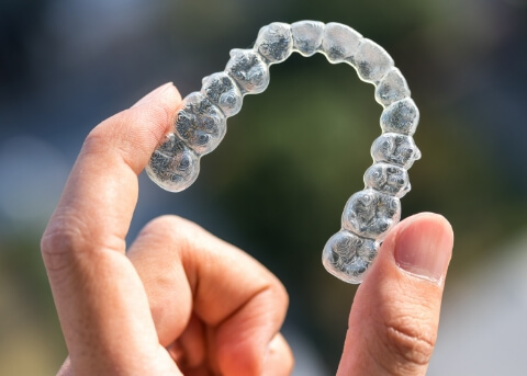 Close up of a hand holding a clear aligner