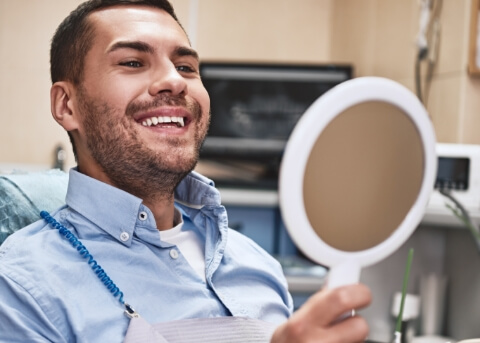 Dental patient looking at his smile in a hand mirror