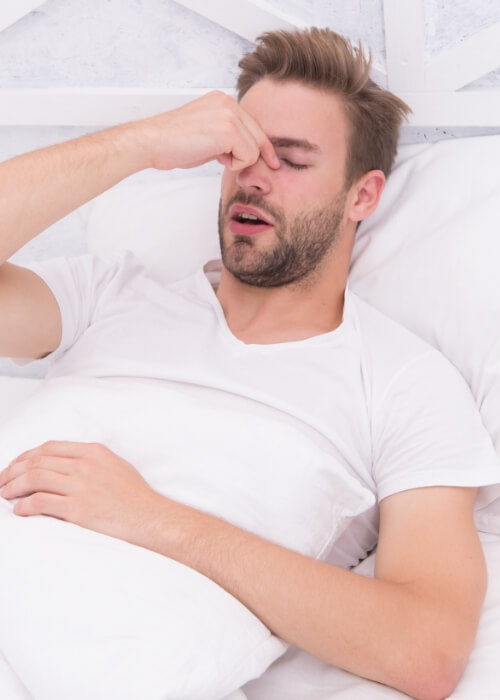 Man laying in bed and pinching the bridge of his nose before sleep apnea treatment in Cumming