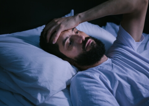 Man laying awake in bed with his hand on his forehead