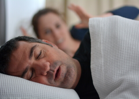 Frustrated woman in bed glaring at snoring man next to her