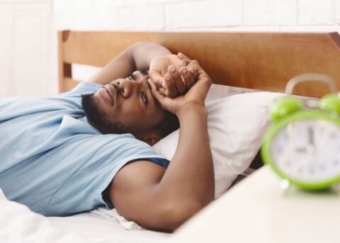 Man laying awake in bed with alarm clock on nightstand reading 9 o clock