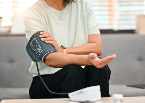Person sitting on couch and putting blood pressure cuff on their arm