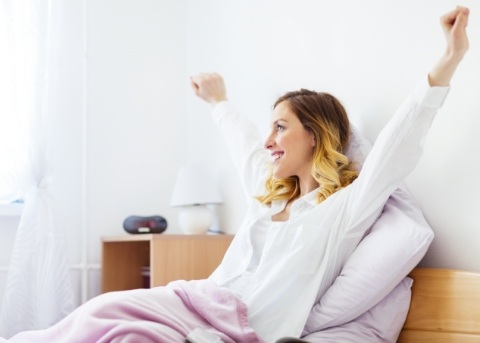 Smiling woman sitting up in bed and stretching
