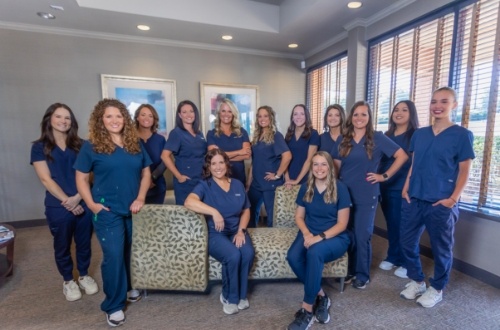 Cumming dental team members in tan and dark blue dresses in front of Bragg Dental office