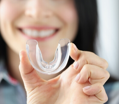 Smiling woman holding a clear occlusal splint tray