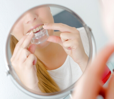 Woman looking in mirror and placing a clear tray over her teeth