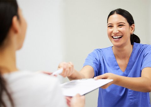 Dental assistant smiling while handing patient form