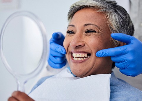 Woman smiling while looking at reflection in handheld mirror