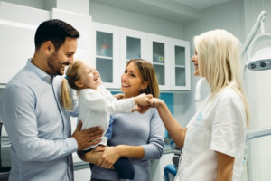 Little girl shaking dentist’s hand while parents hold her