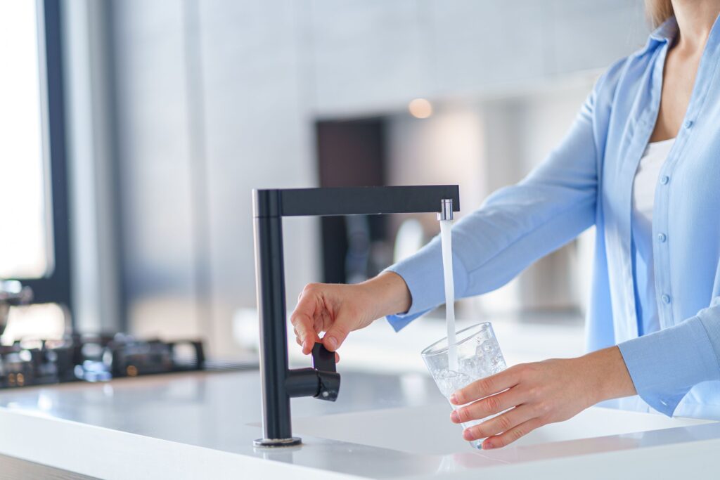 Neck-down view of woman in blue shirt filling glass at kitchen sink